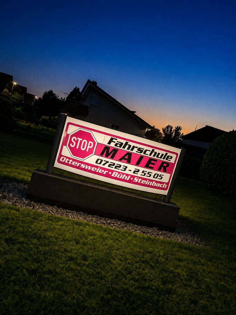 Beleuchtetes Schild der Fahrschule Maier in der Abenddämmerung